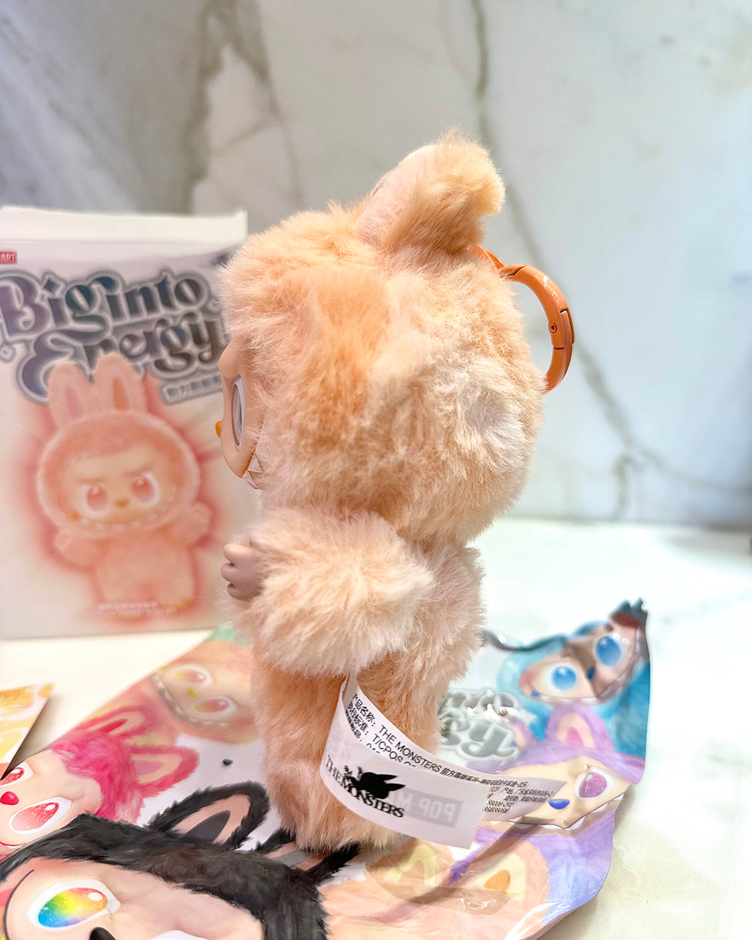 Plush toy with a strap on a surface with colorful packaging in the background