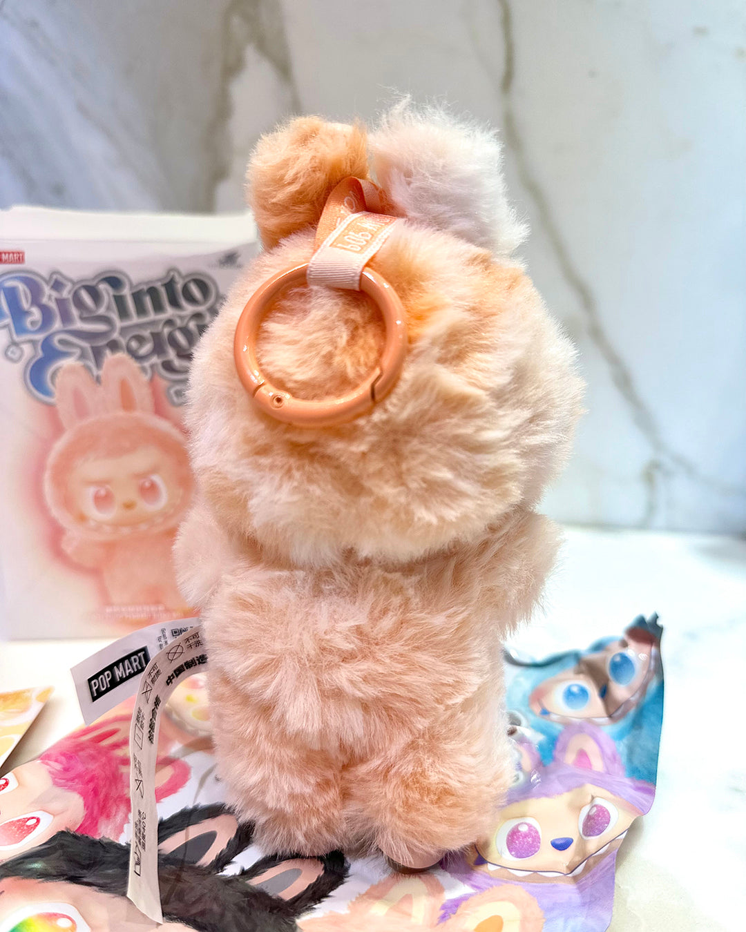 Plush toy with a ring on top, sitting on a surface with colorful packaging in the background.