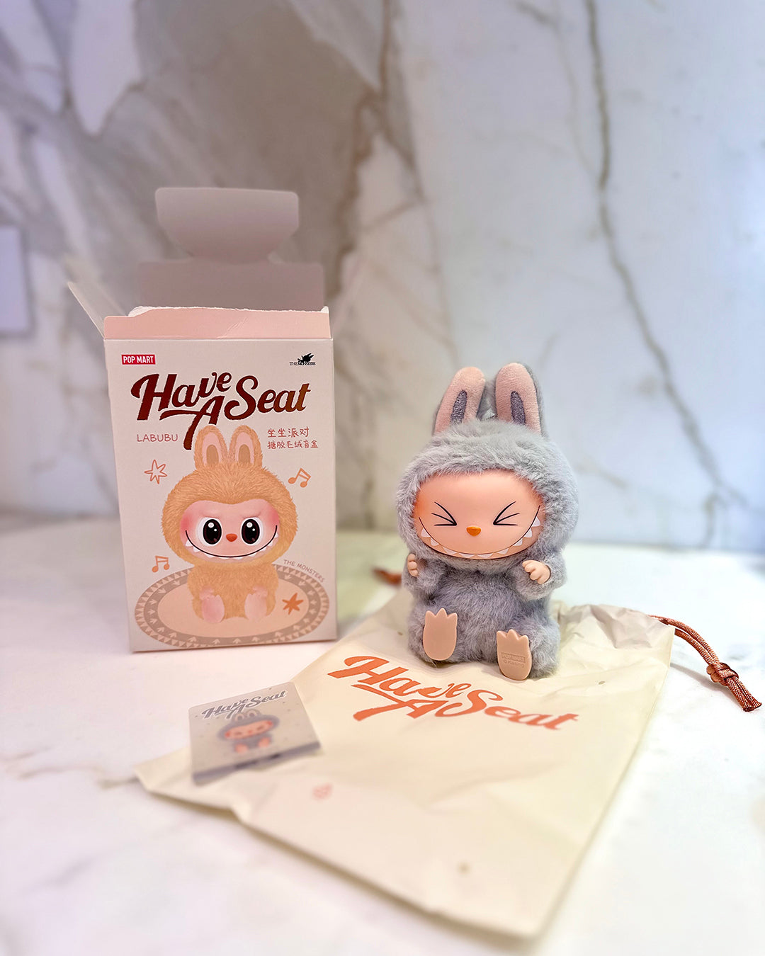 Plush toy with packaging and branded pouch on a light background