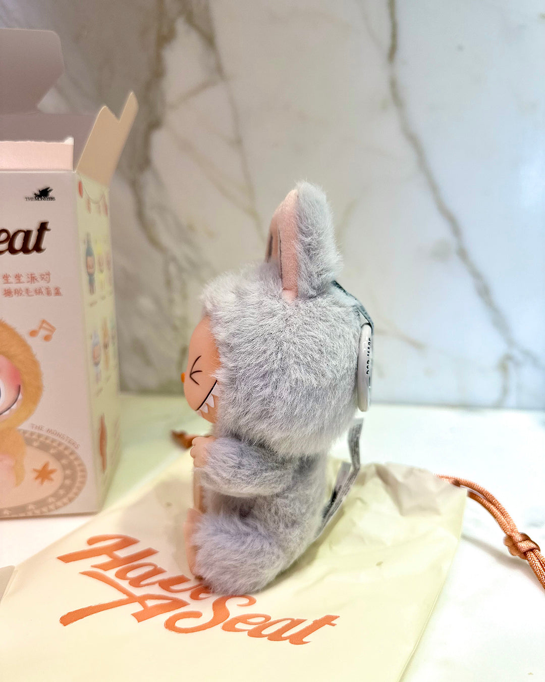 Plush toy with rabbit ears next to a box of 'Great Seat' on a white surface.