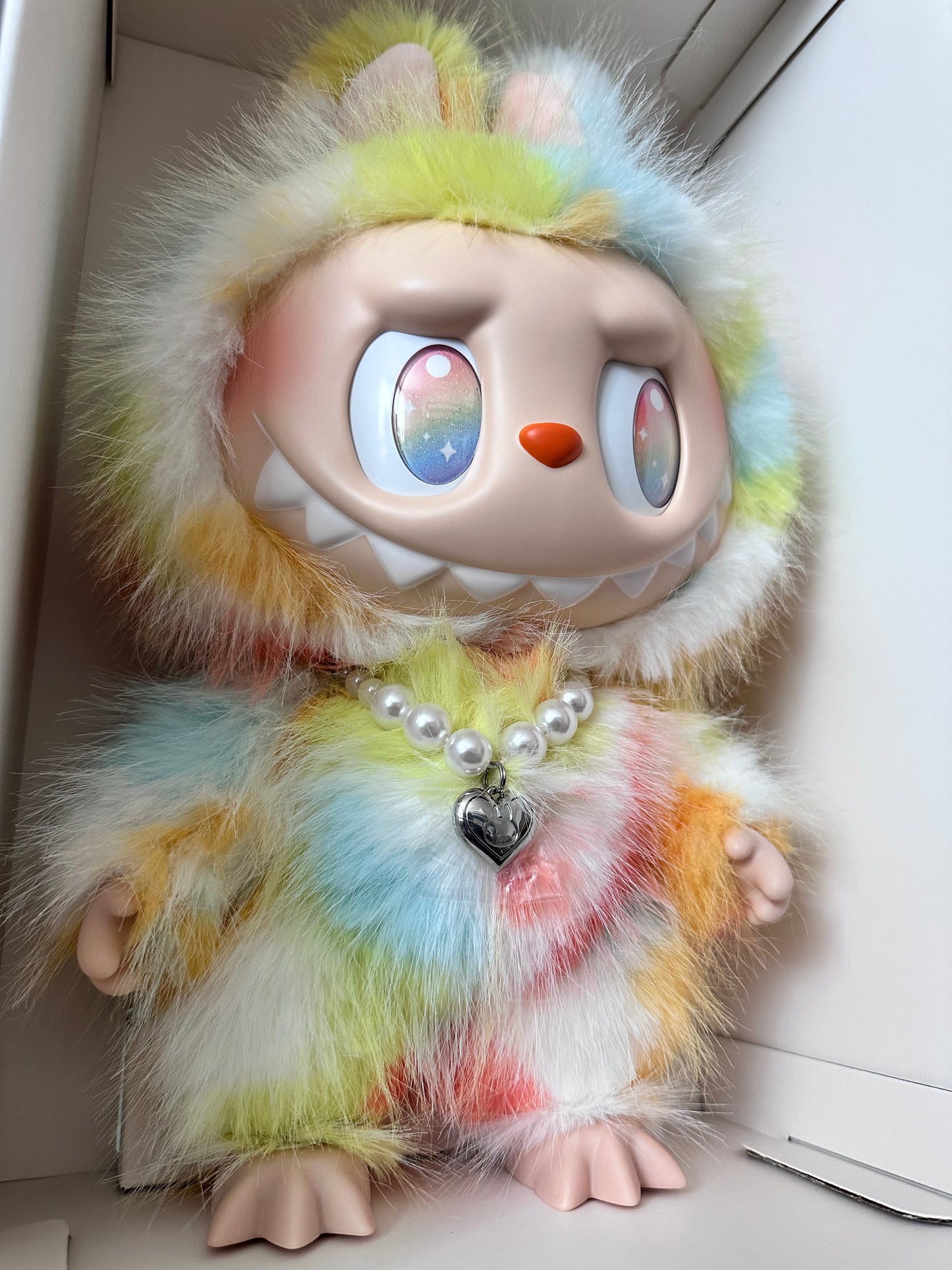 Toy figure with colorful fur and a pearl necklace on a plain background