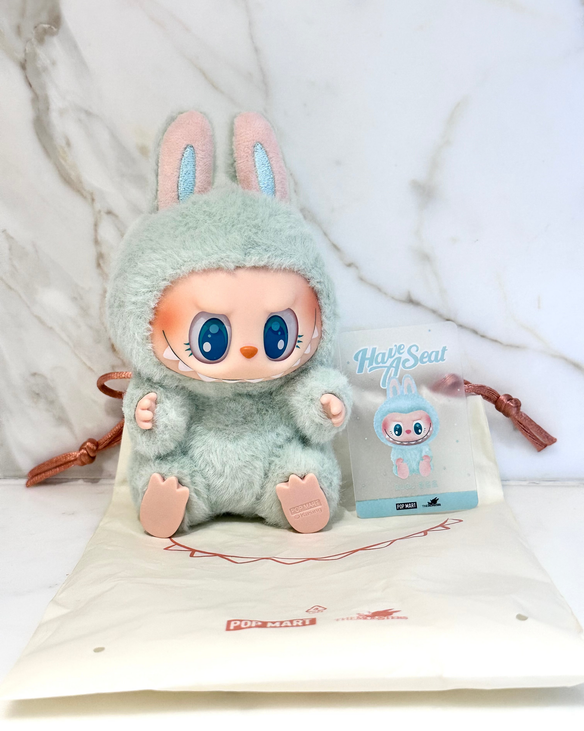 Plush toy with bunny ears and a small bag with branding on a white background