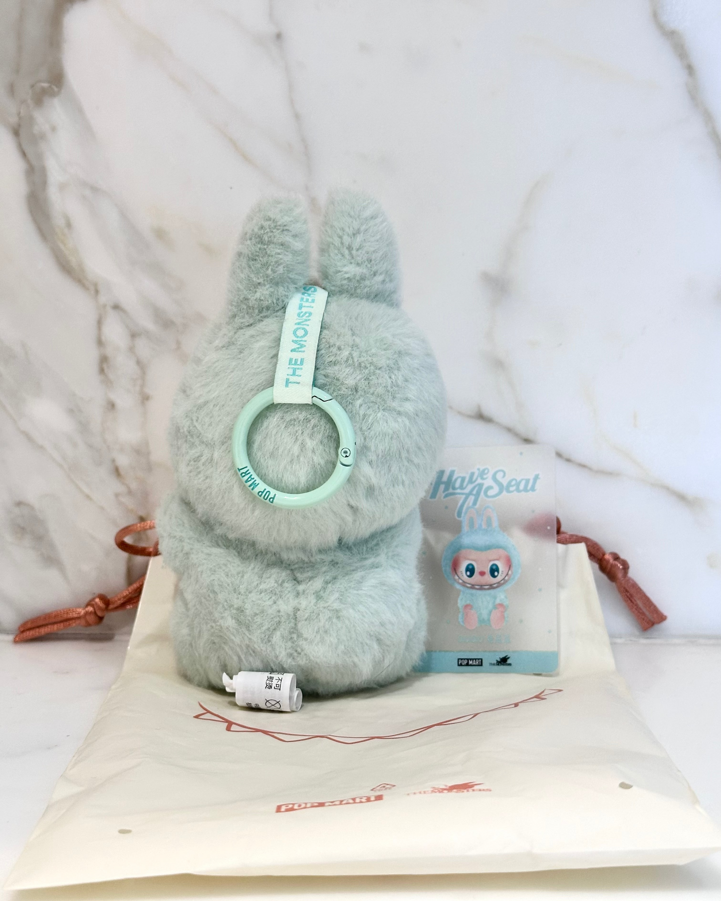 Plush toy with a green band and packaging on a marble surface