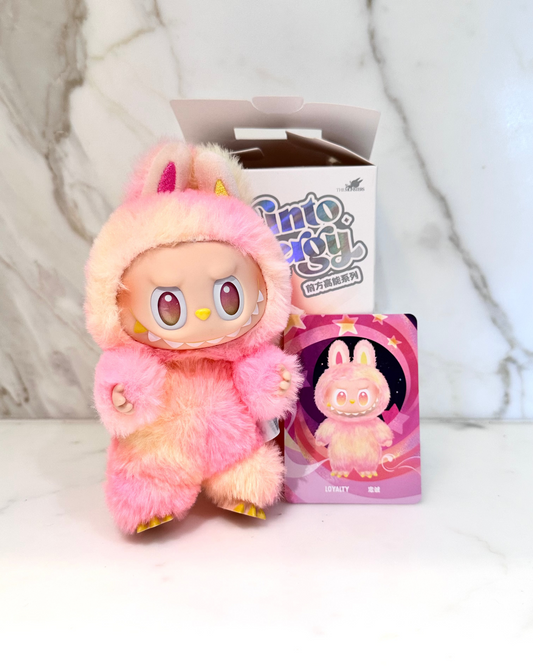 Pink plush toy with a box and card featuring the same design on a light gray background