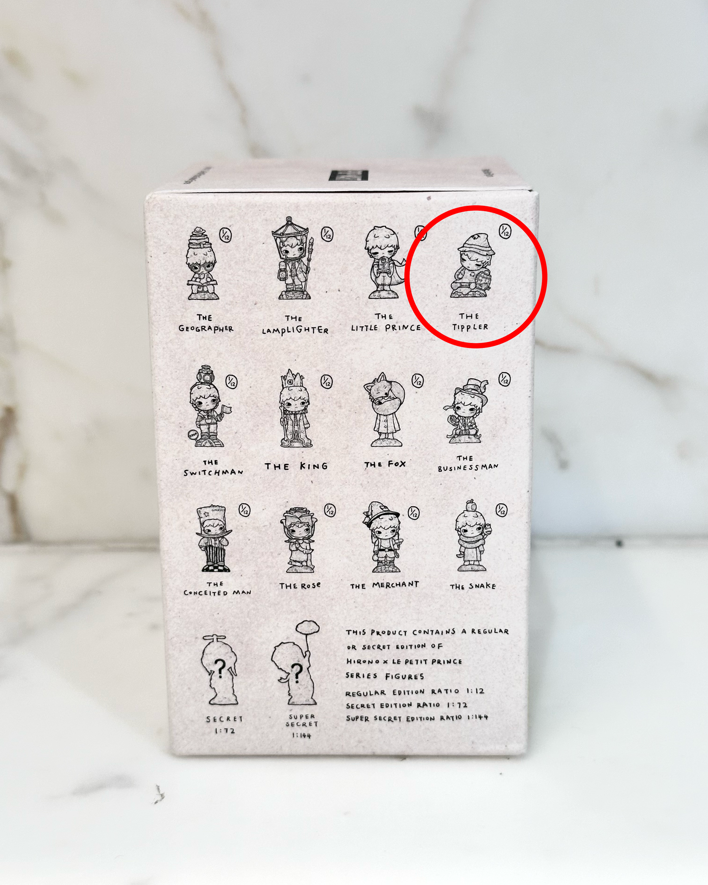 Box with illustrations of small figures and a red circle highlighting one of them on a marble background.