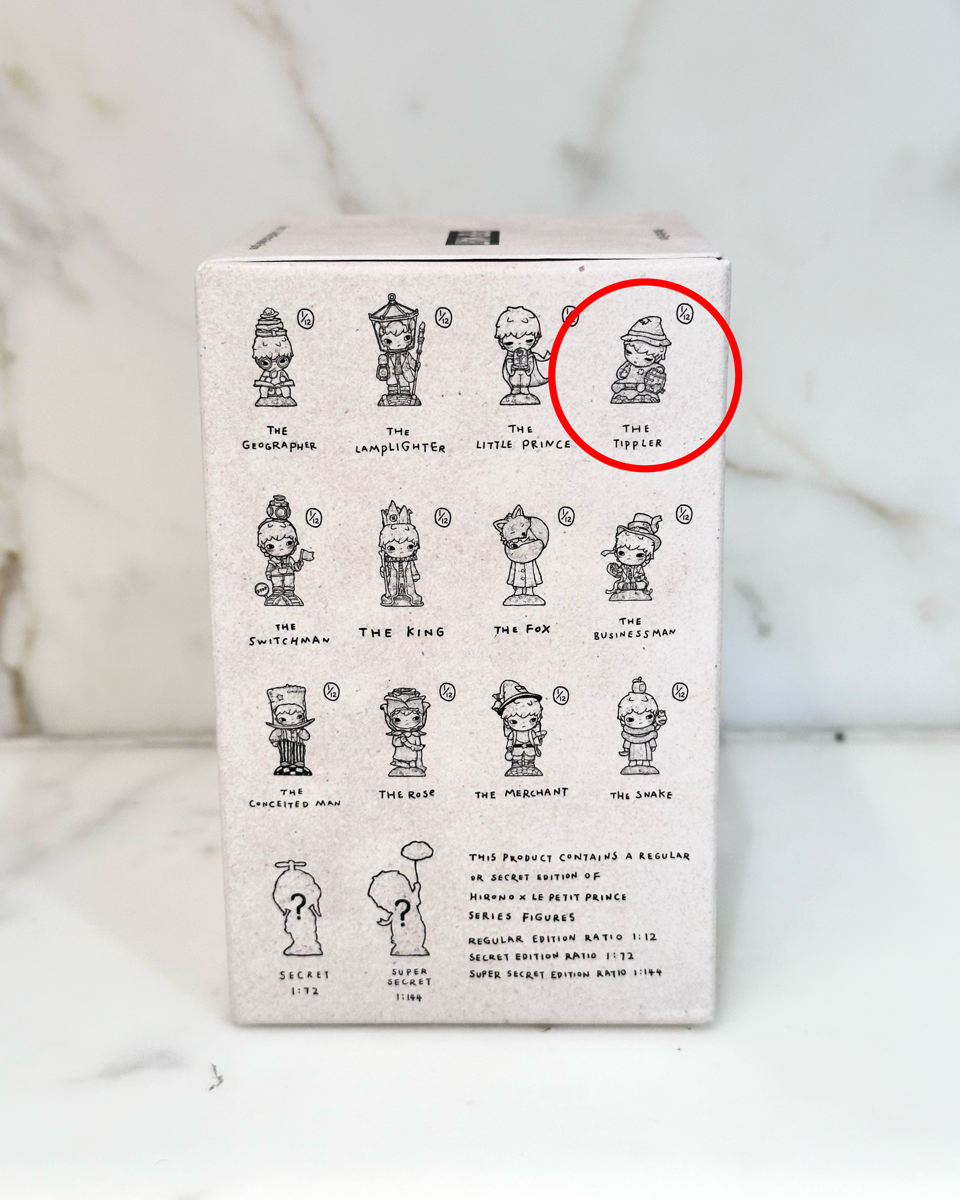 Box with illustrations of small figures and a red circle highlighting one of them on a marble background.