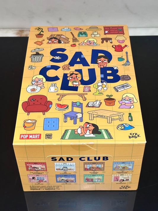 Box of 'Sad Club' with colorful illustrations on a dark surface