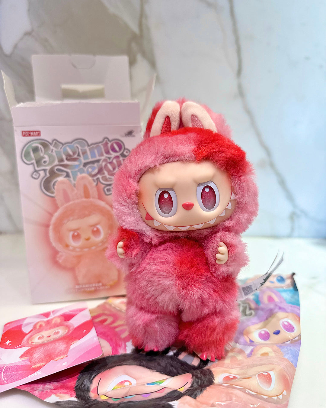 Pink plush toy with bunny ears on a white surface with promotional material in the background