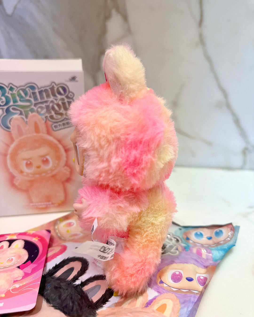 Colorful plush toy with a book and cards on a white surface