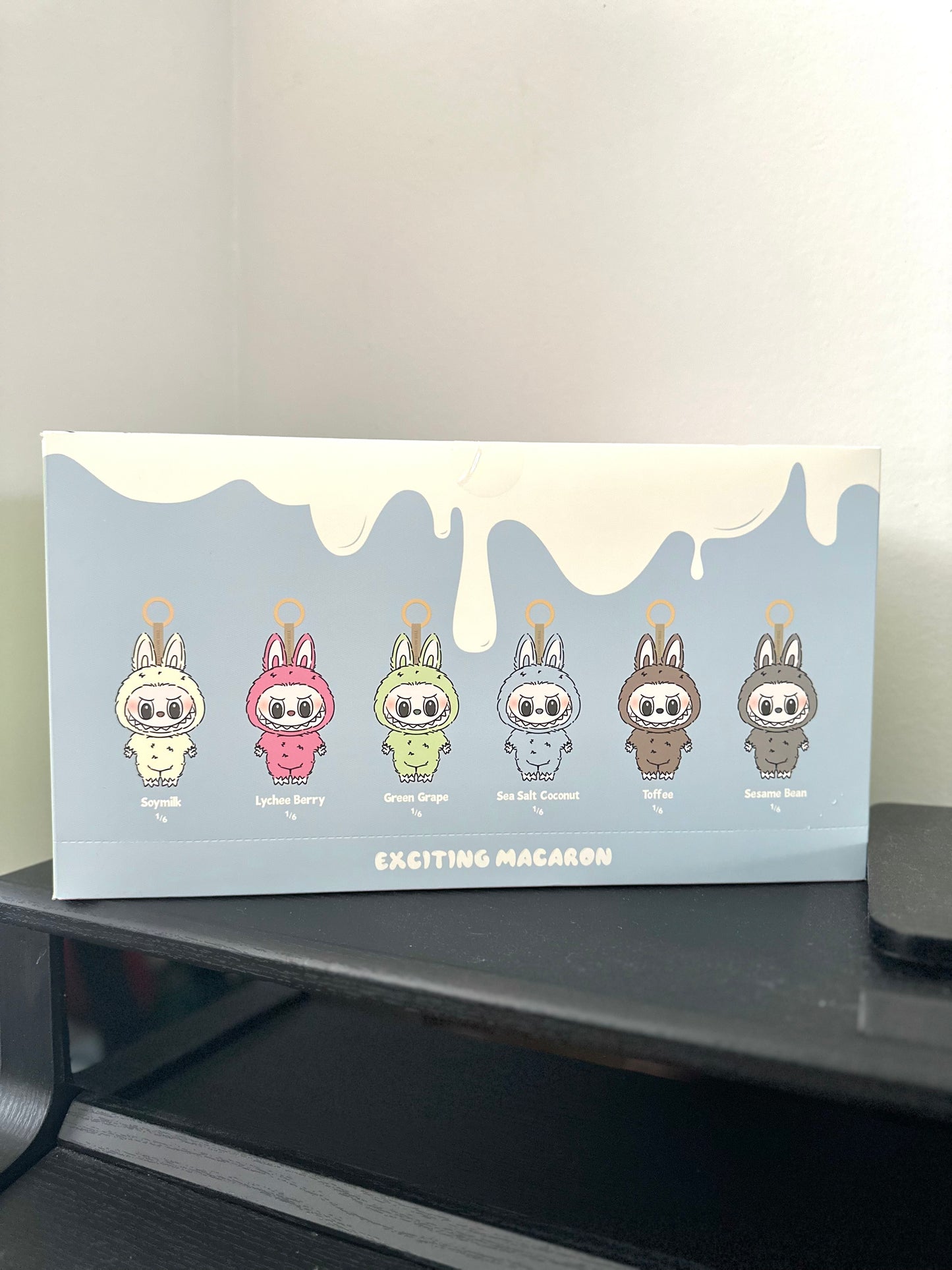 Box of 'Exciting Macaron' with cartoon character designs on a black surface.