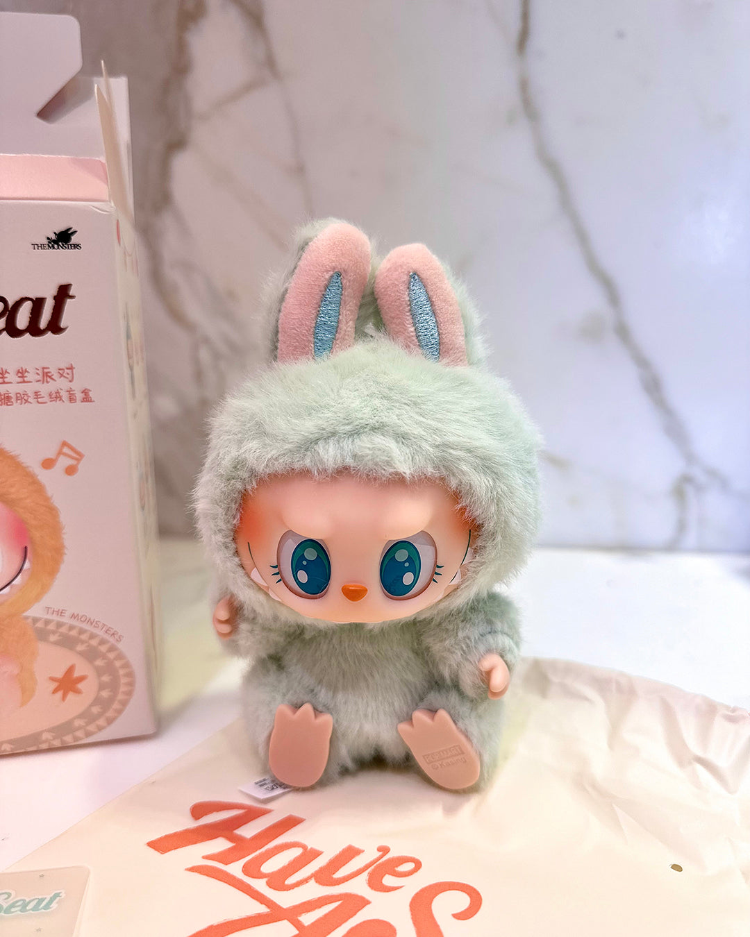 Toy figure with bunny ears and green outfit next to a box labeled 'Have a Seat'.