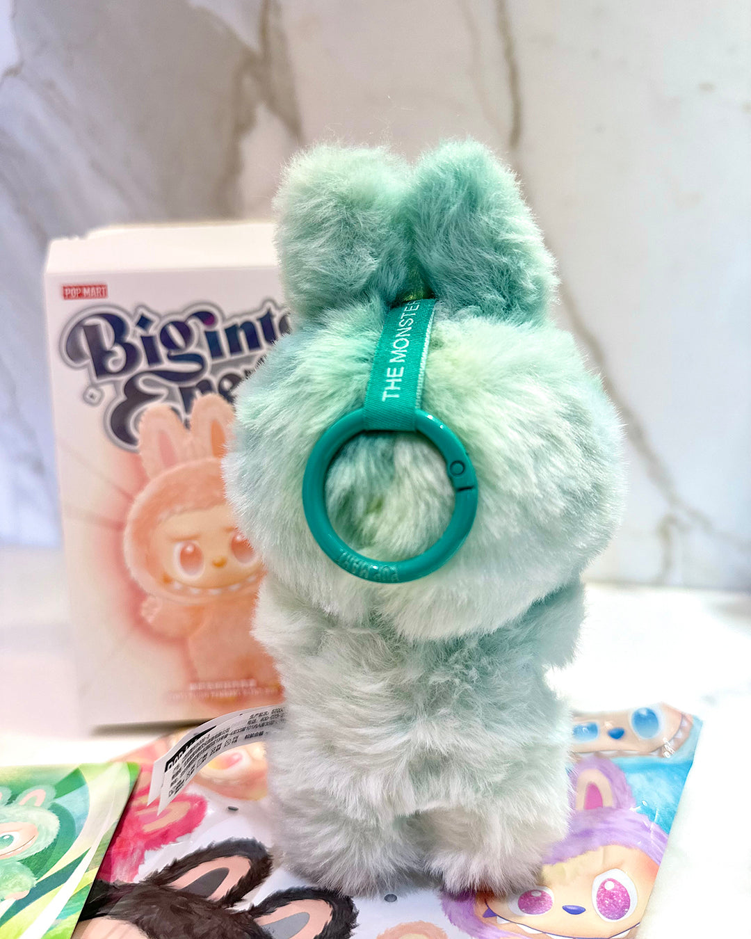 Green plush toy with a ring on a white surface with a box in the background