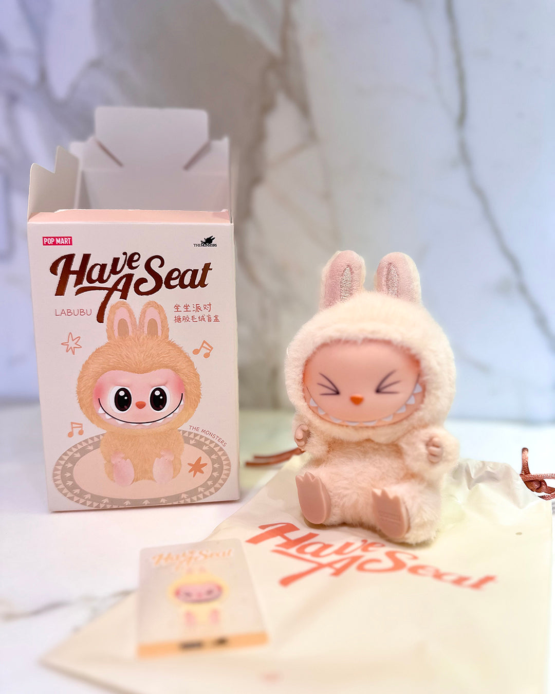 Plush toy and packaging with 'Have A Seat' branding on a light background