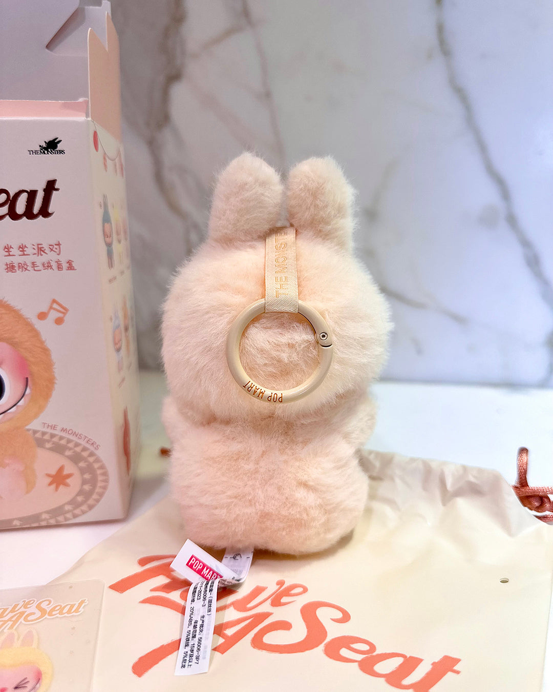 Plush toy with a circular object, next to a box labeled 'The Little Seal', on a light background.