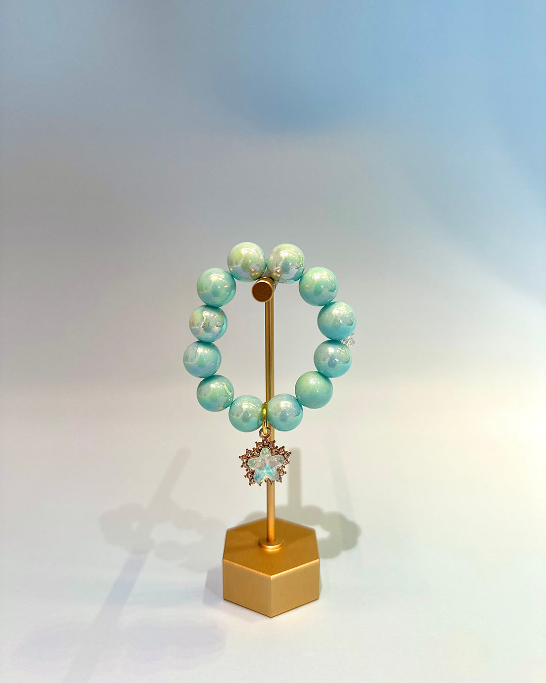 Turquoise beaded bracelet on a gold stand with a light blue background