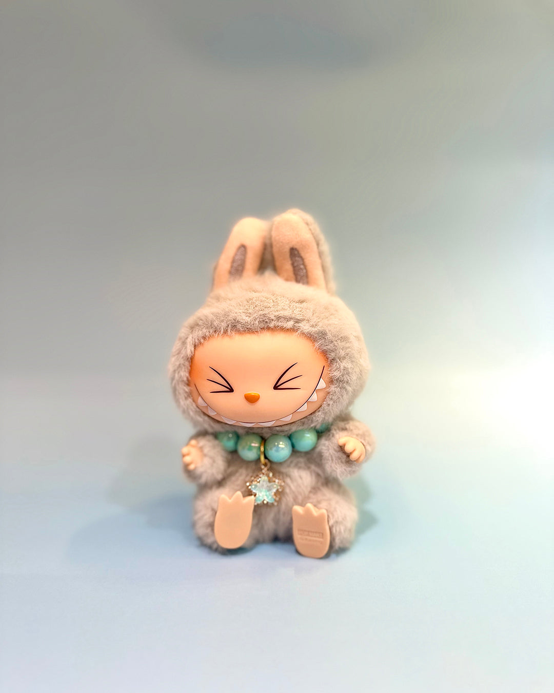 Plush toy with bunny ears and a neutral expression on a light gray background