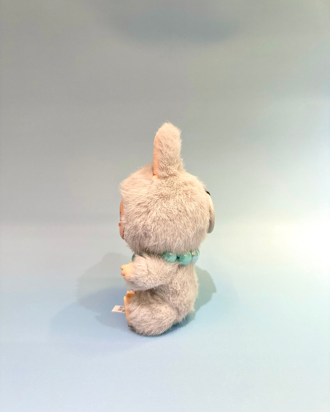 Plush toy resembling a cat with a green ribbon on a light gray background