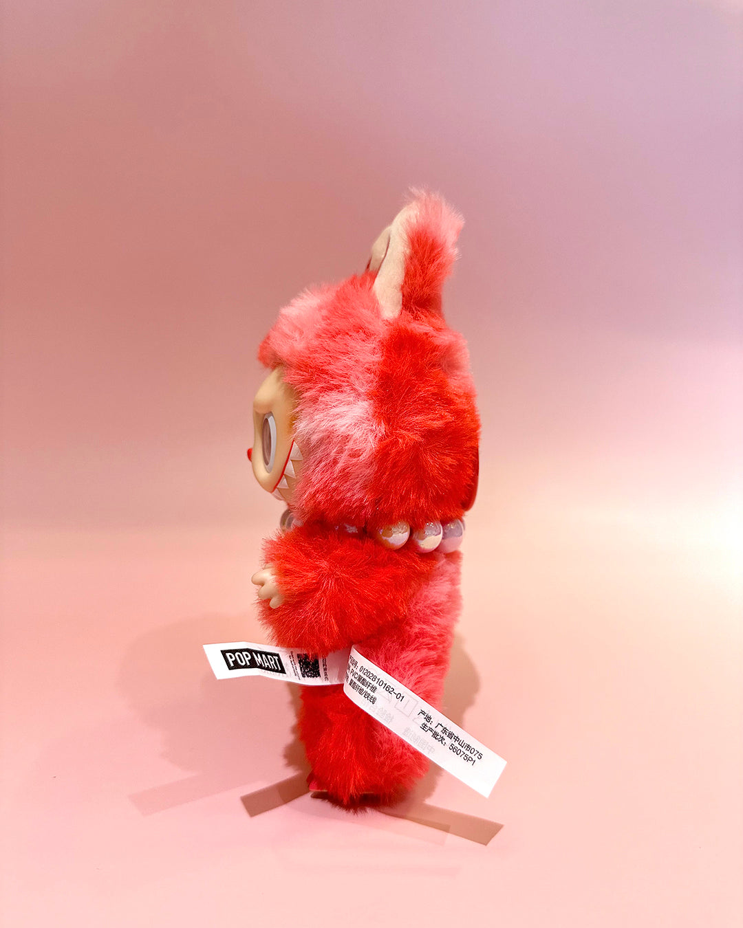 Red plush toy with a beige face on a pink background