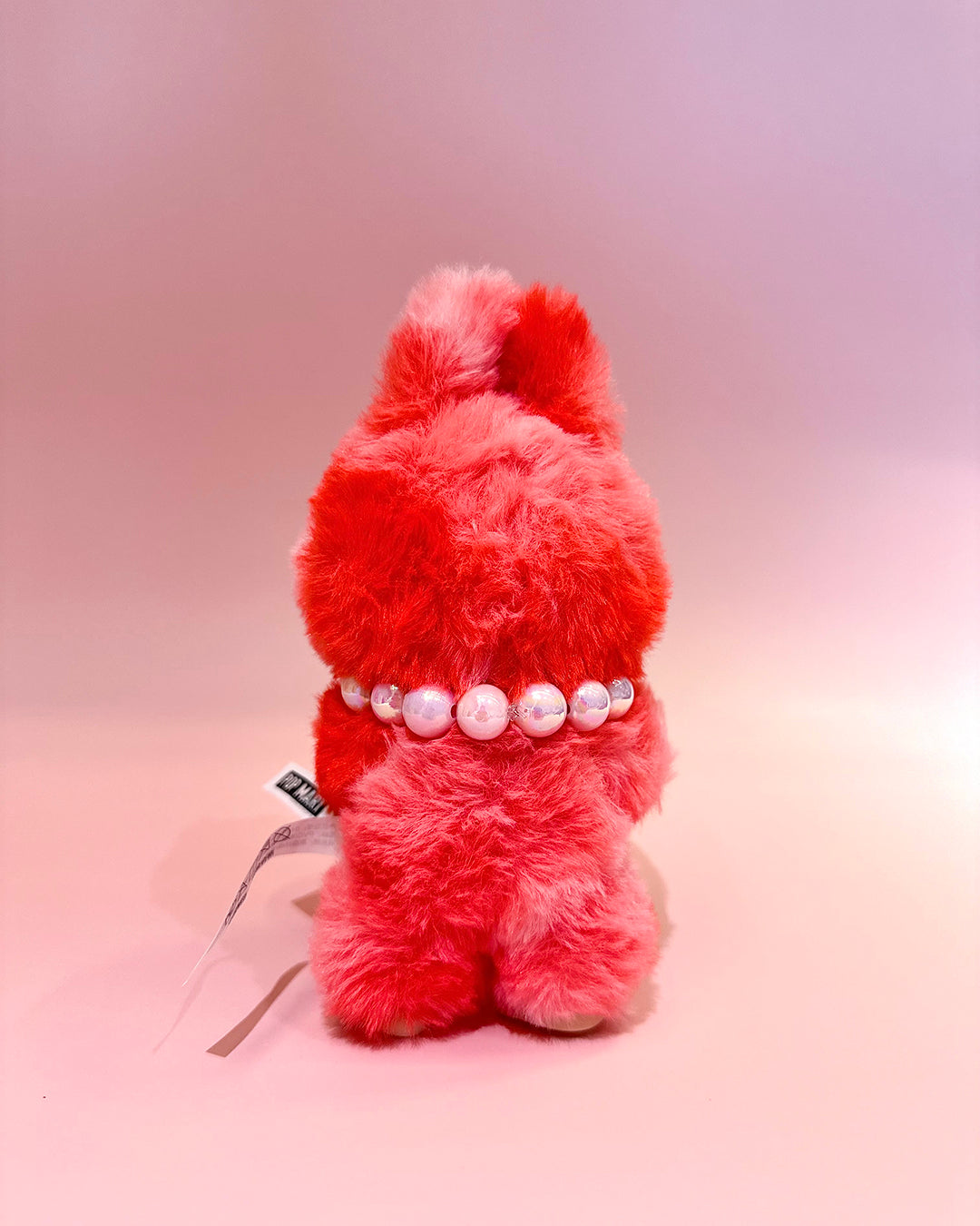 Fluffy red dog toy with a pearl collar on a gradient background