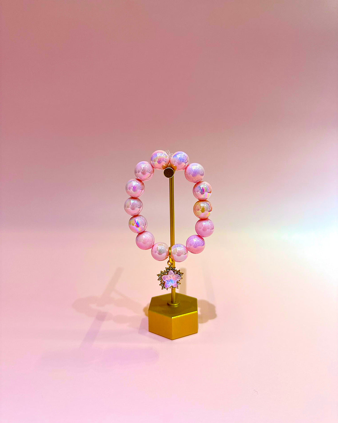 Pink beaded bracelet on a gold stand against a gradient pink background