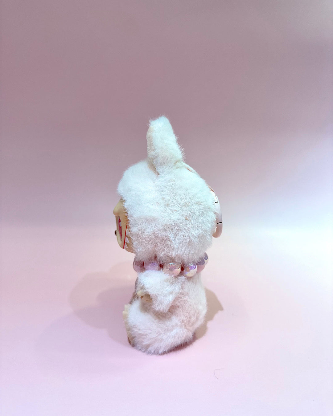 Small white plush toy with a fluffy texture on a light pink background