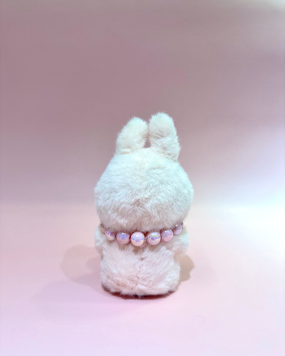 White fluffy toy with a pink beaded necklace on a light pink background
