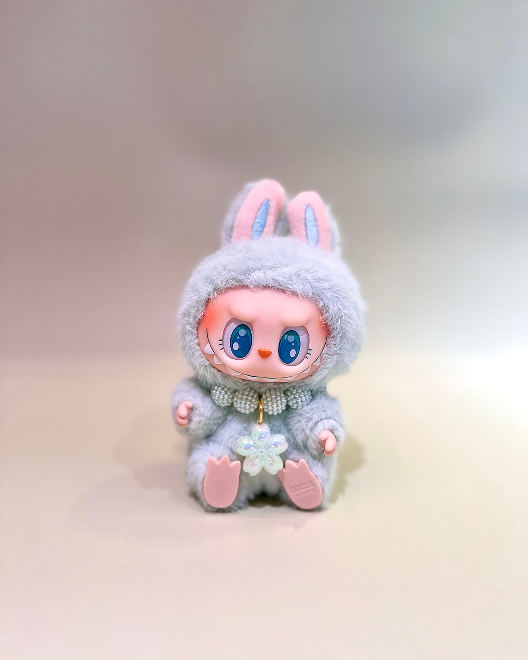 Plush toy with bunny ears and a soft gray outfit on a light background