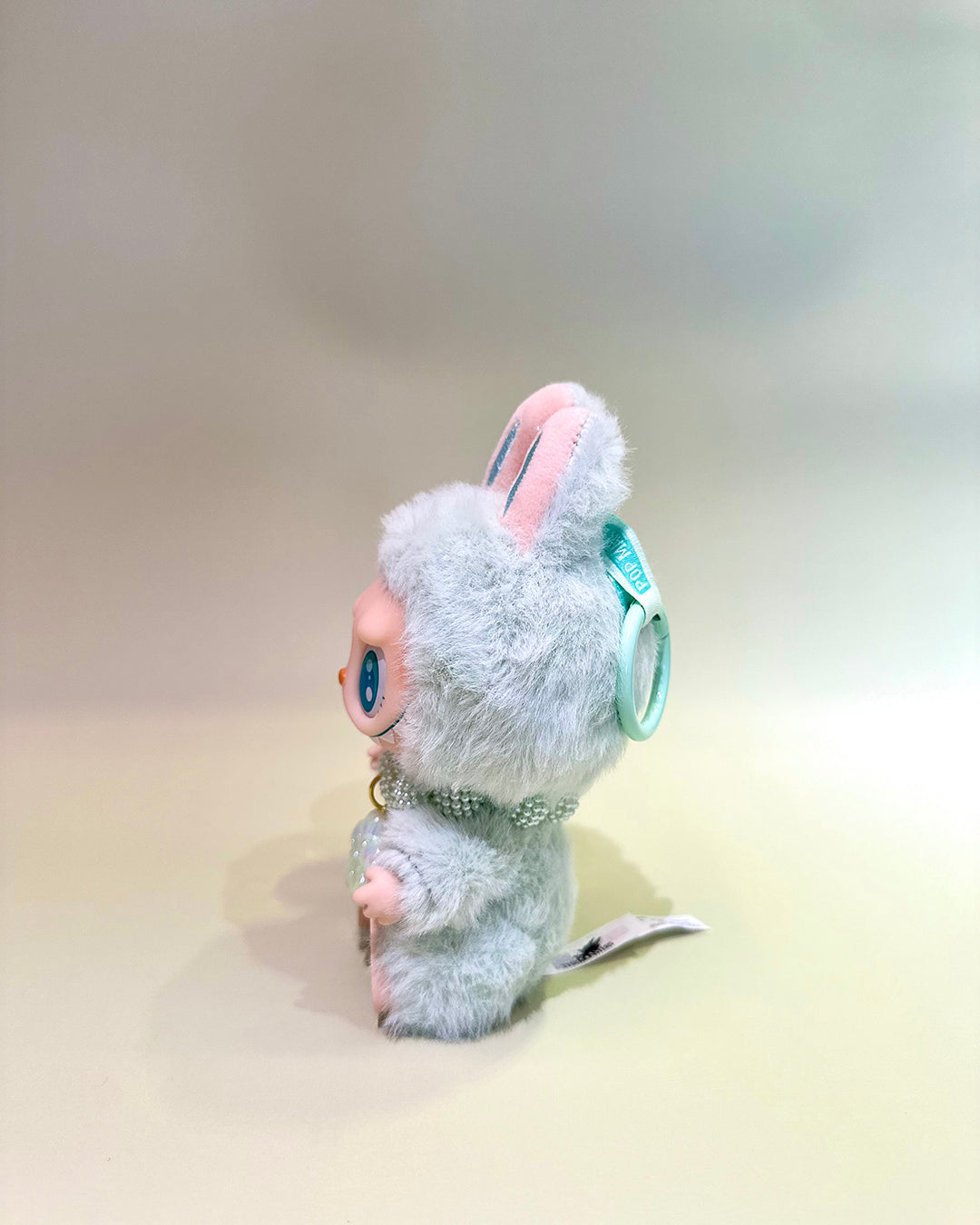 Plush toy resembling a character with a light gray body and pink ears on a beige background