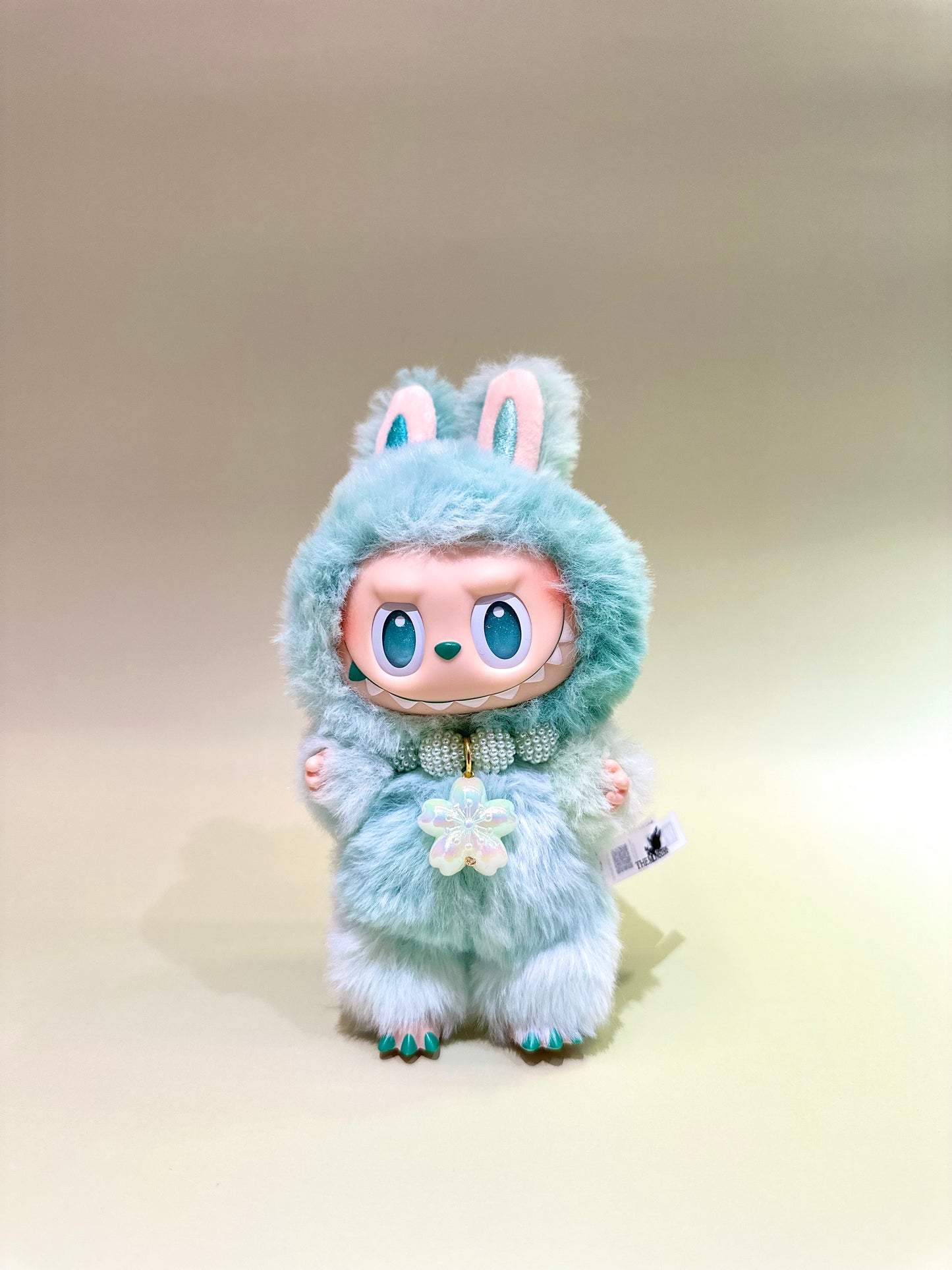 Toy figure with a fluffy green hood and rabbit ears on a beige background