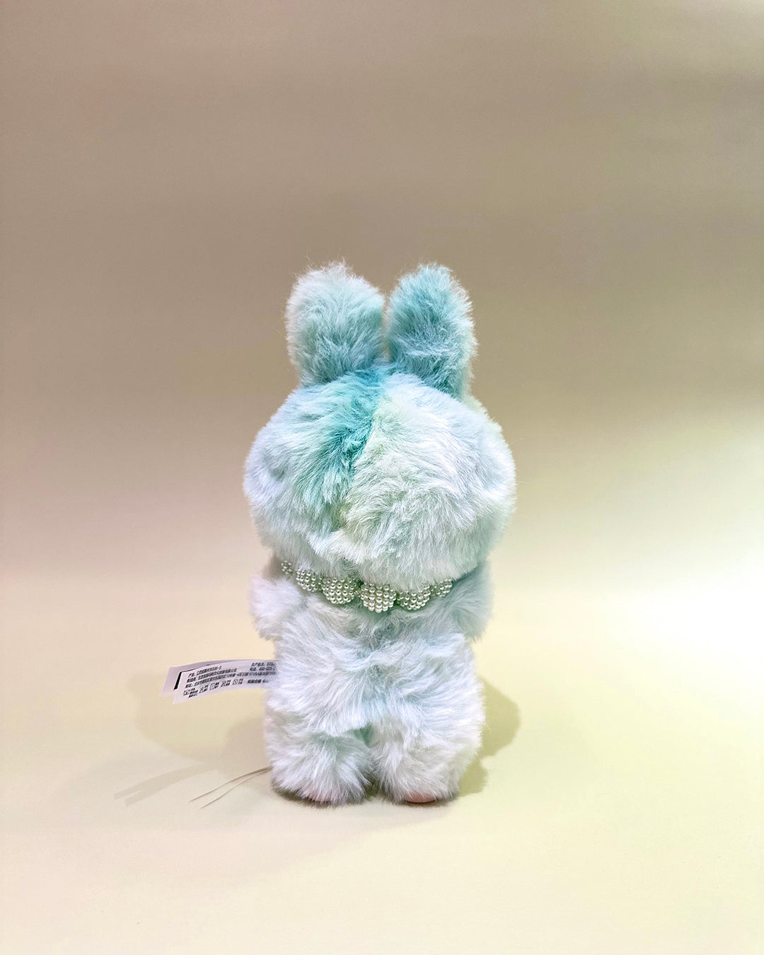 Light blue plush toy with a collar on a beige background