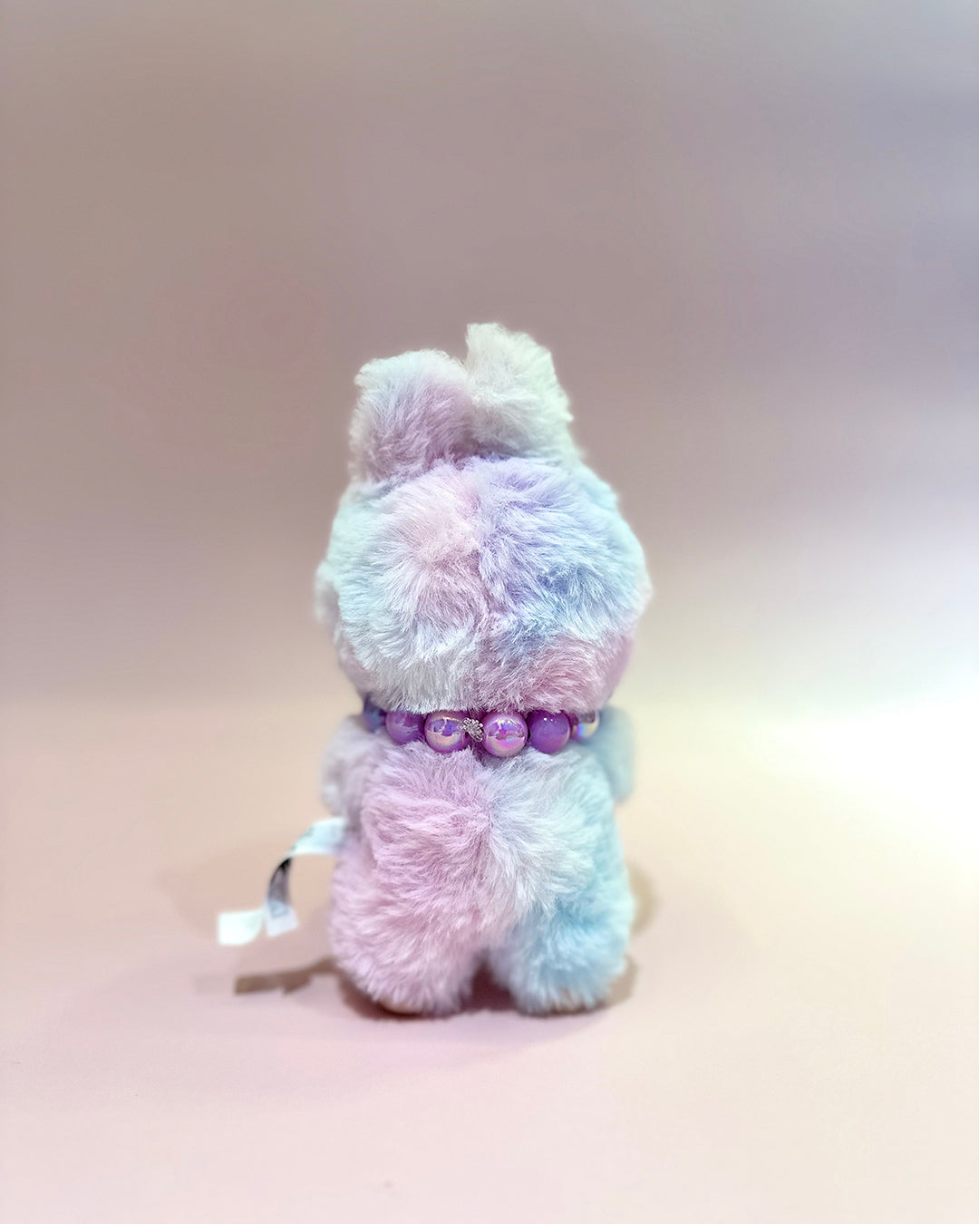 Pastel-colored plush toy with a purple collar on a gradient background