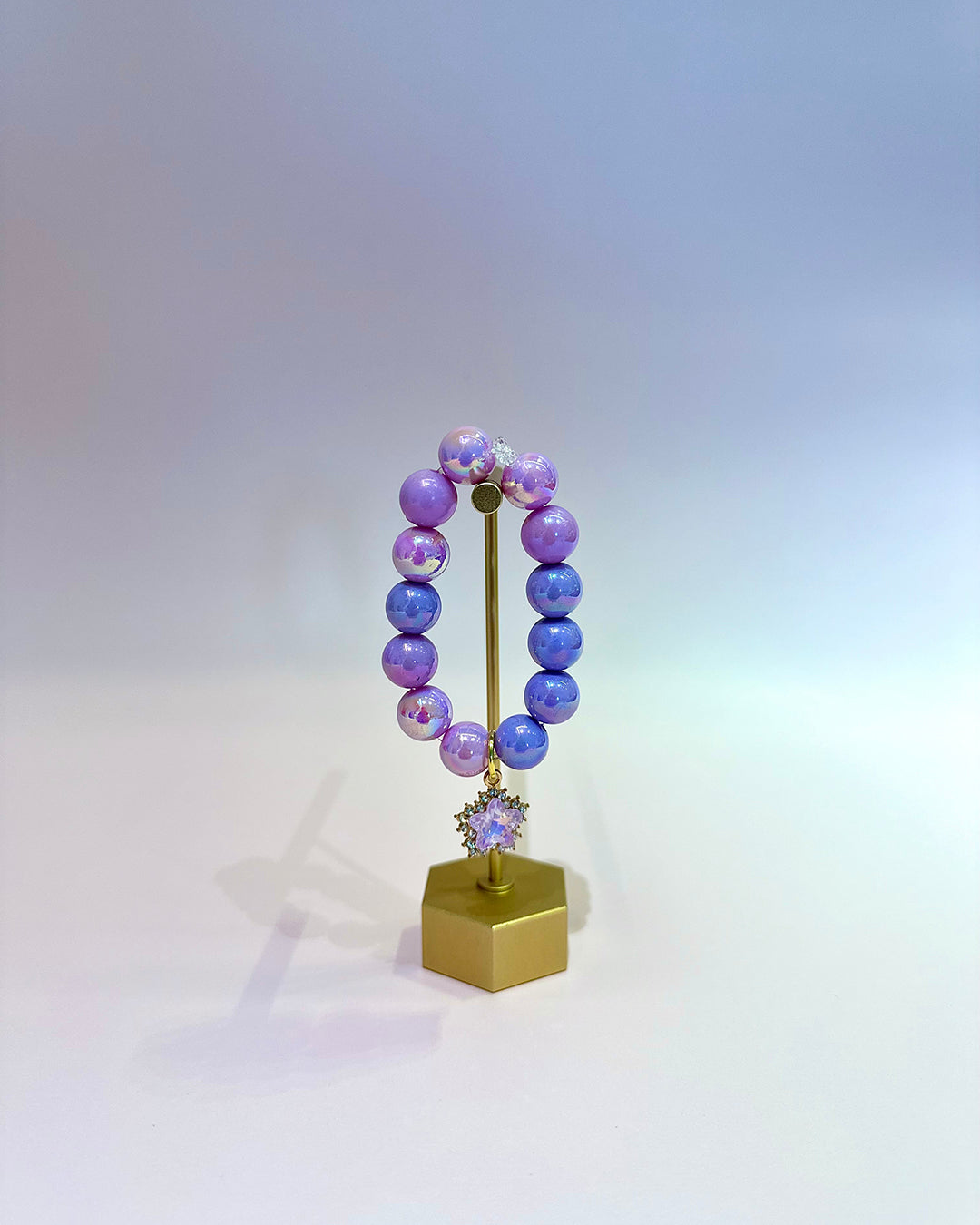 Purple beaded bracelet on a gold stand with a white background