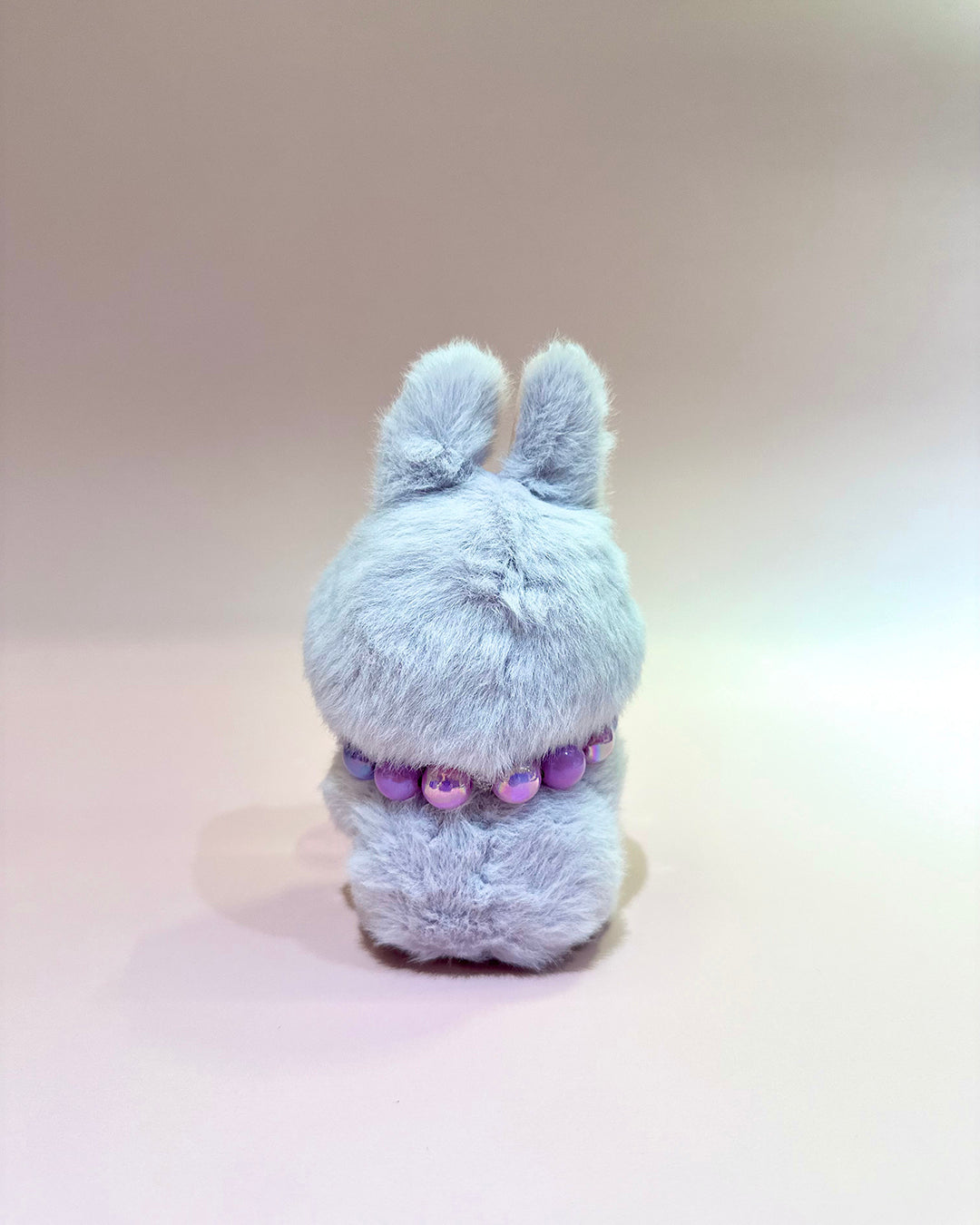 Plush toy with a purple beaded necklace on a beige background
