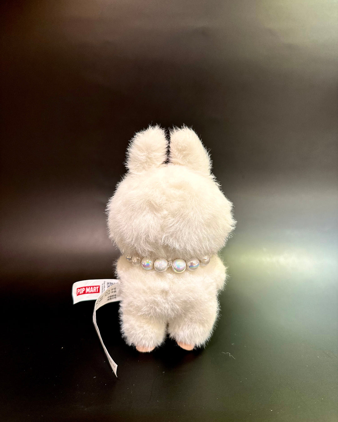 White plush toy with pearl necklace on a dark surface