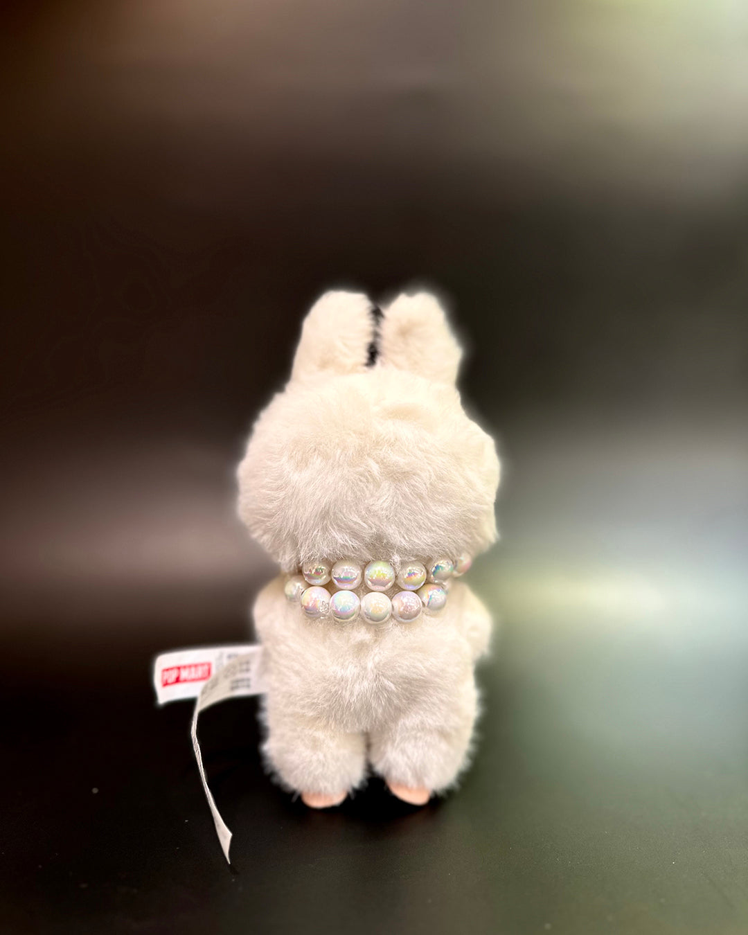 White plush toy with a pearl necklace on a dark background