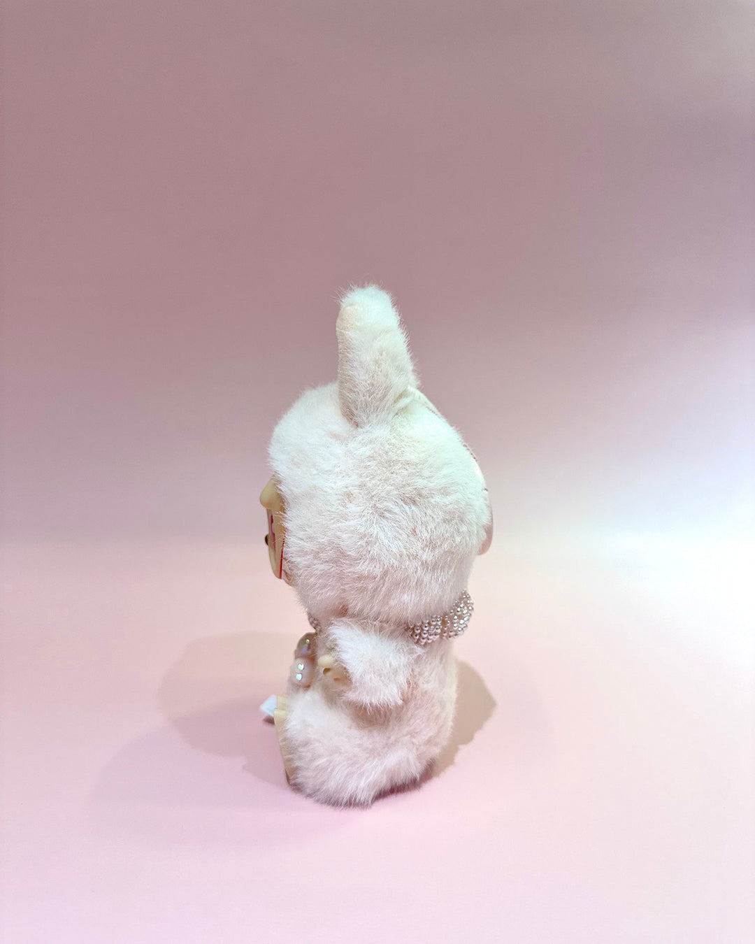 White fluffy toy with a decorative belt on a pink background