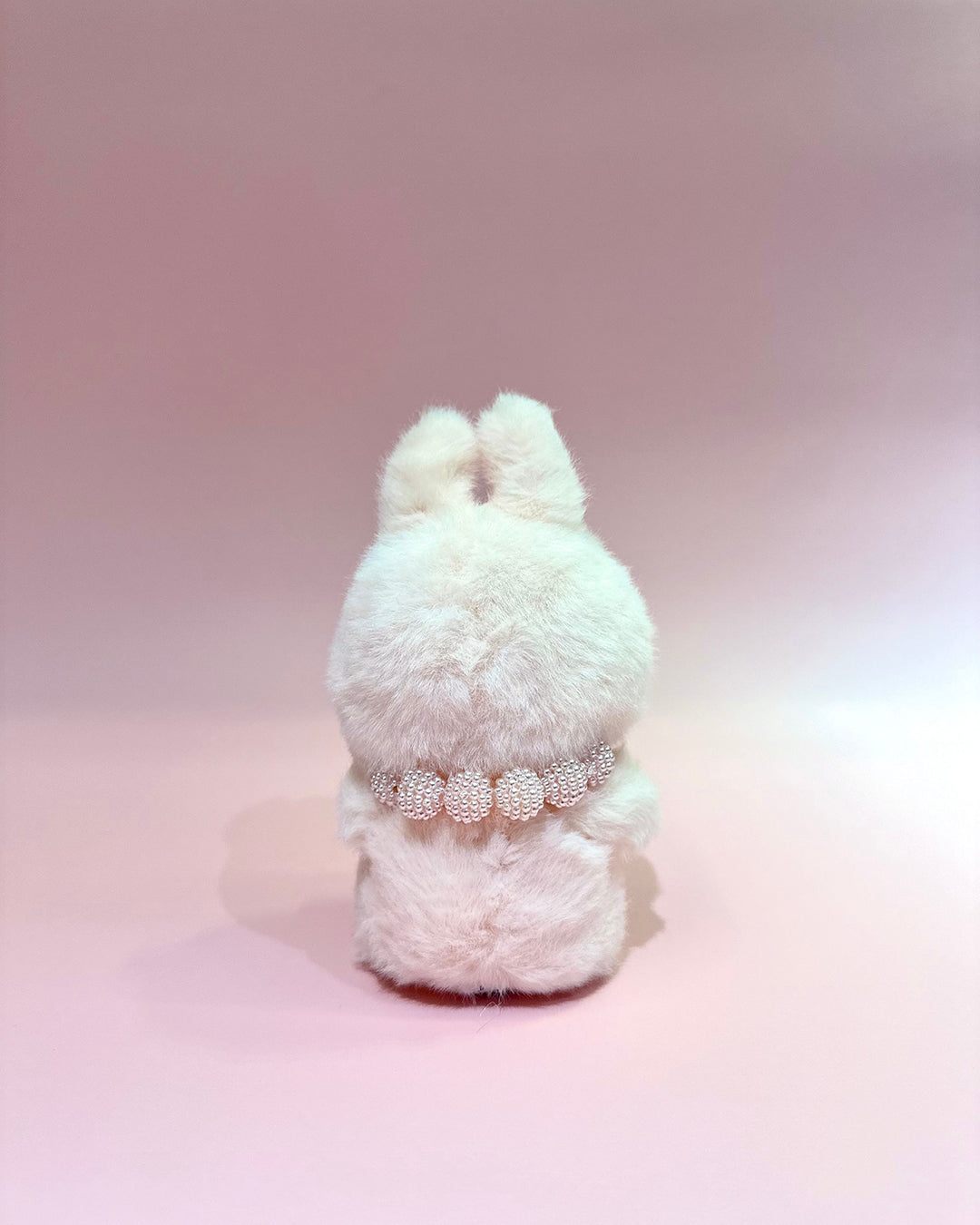 White fluffy toy with a decorative belt on a pink background