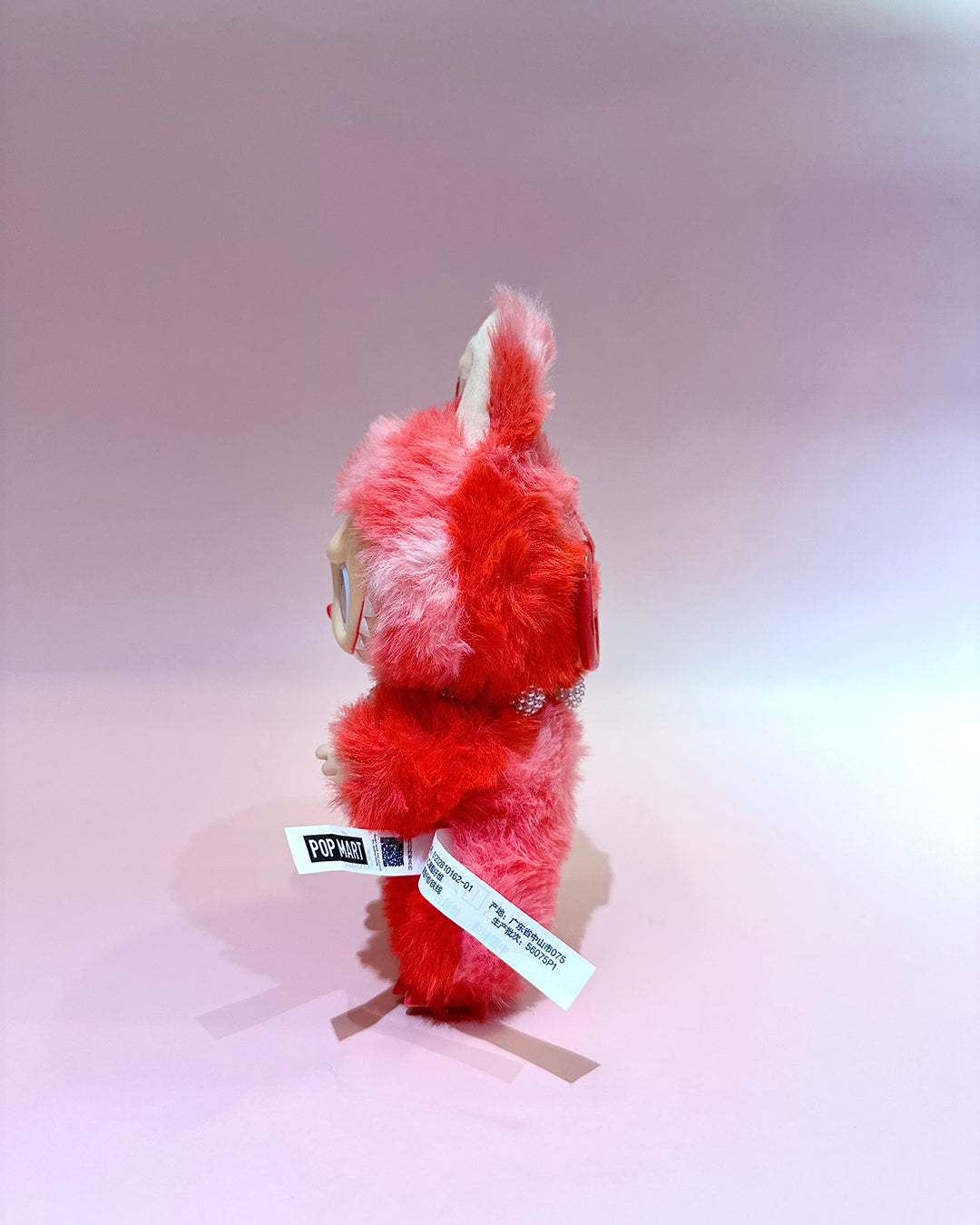 Red and white plush toy with tags on a light gray background