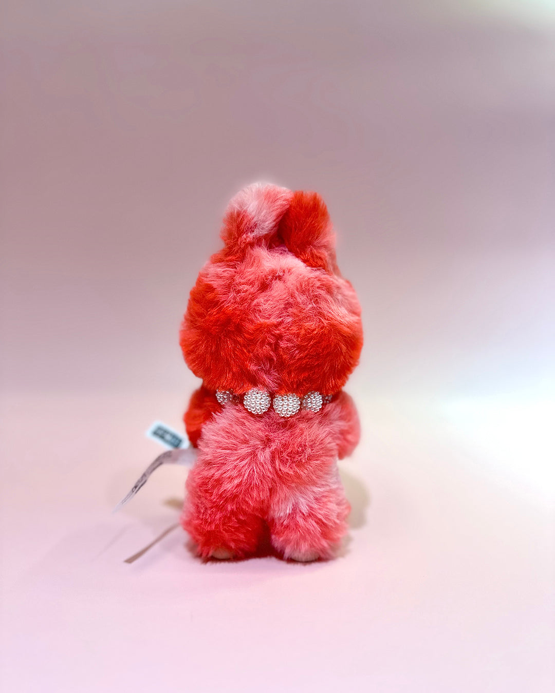 Red plush toy with a decorative belt on a light gray background