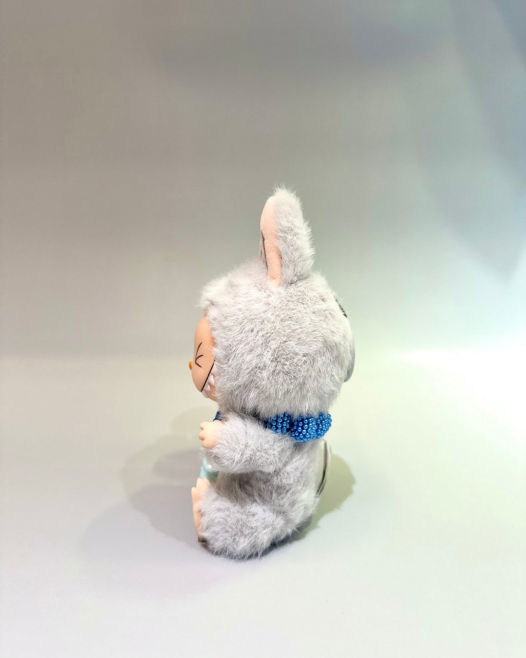 Plush toy resembling a rabbit with a blue scarf on a light gray background