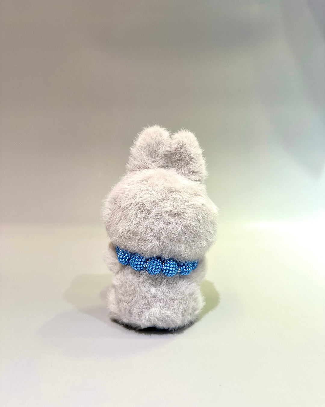 Gray plush toy with a blue collar on a light gray background
