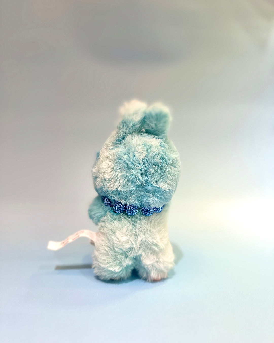 Light blue plush toy with a blue collar on a white background