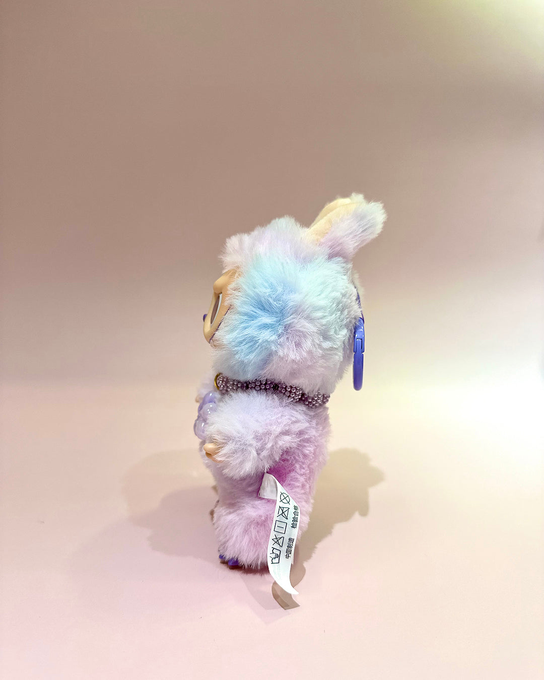Multicolored plush toy with a tag on a beige background