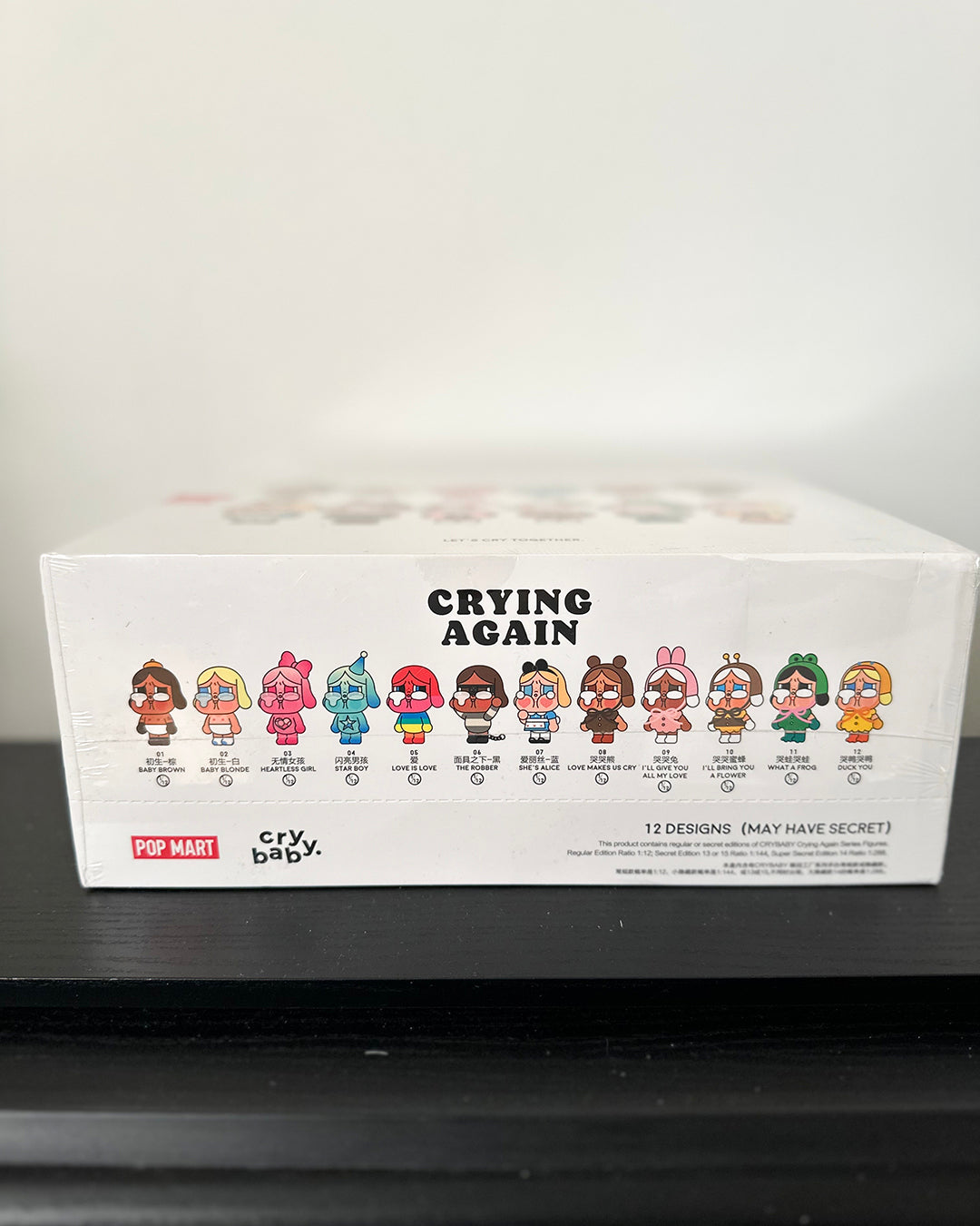 Box of 'Crying Again' figurines by Pop Mart on a black surface with a white background