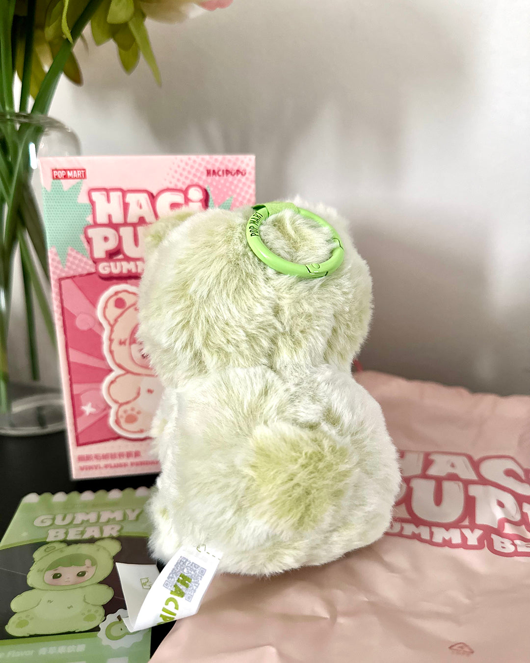 Fluffy white toy with a green tag in front of a pink box labeled 'HAGI PUPPY GUMMY' on a blurred background.