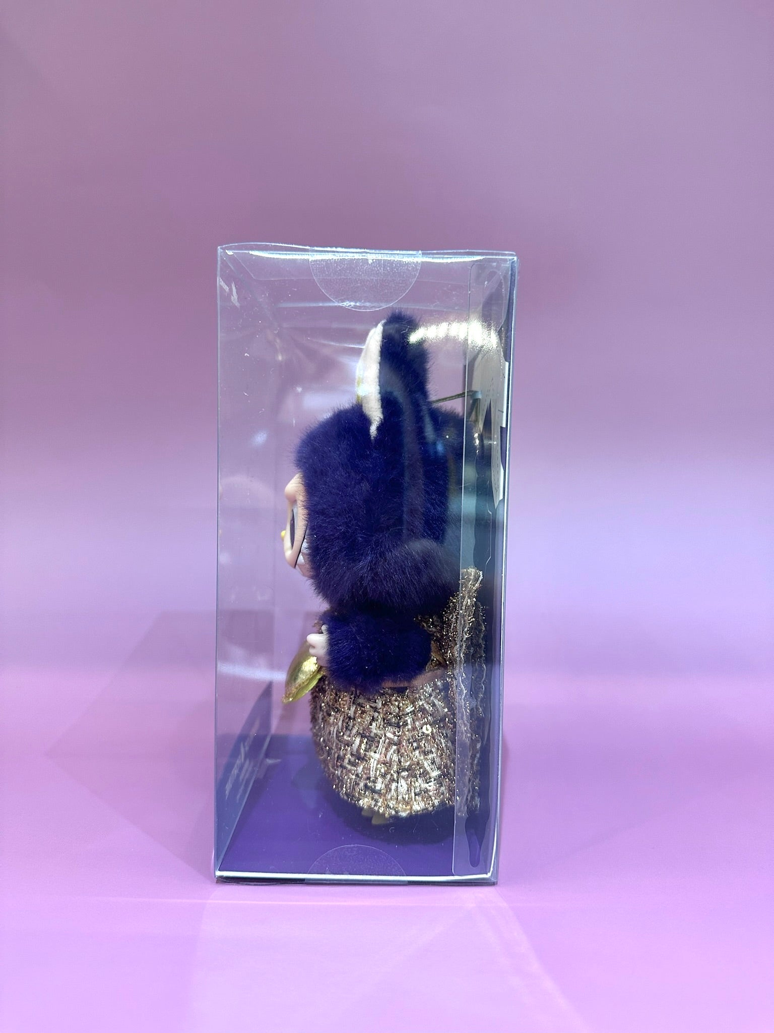 Decorative item with blue pom-poms and gold accents in a clear box on a pink background