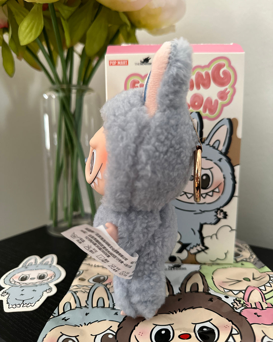Plush toy with a keychain attached, displayed in front of a box with cartoon characters.