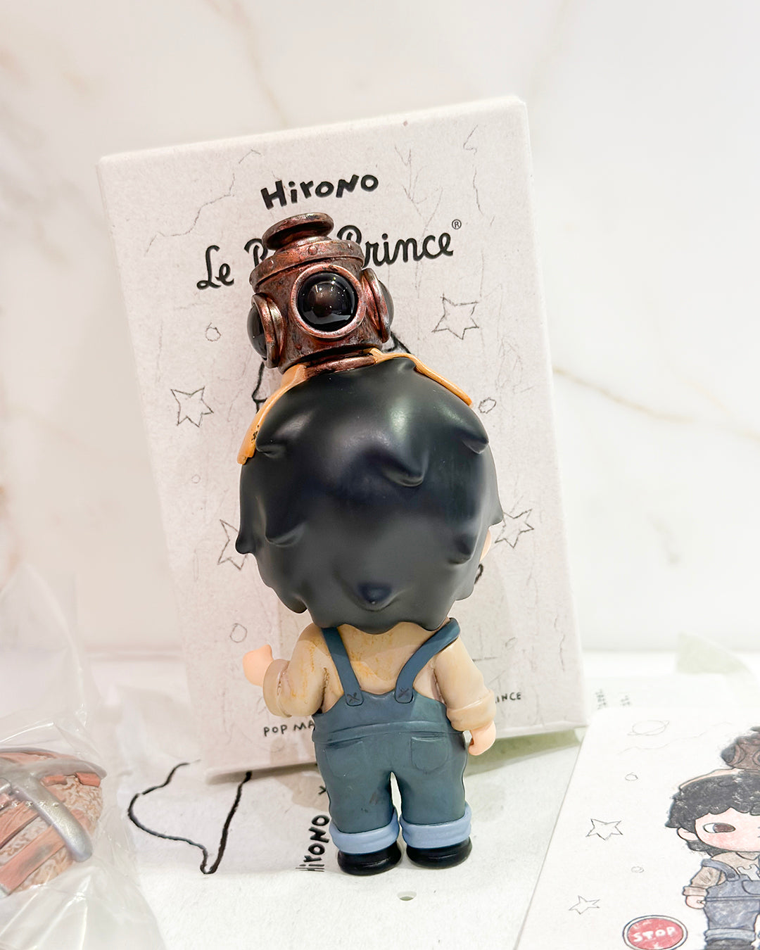 Toy figure of a child wearing a helmet and overalls on a branded stand.