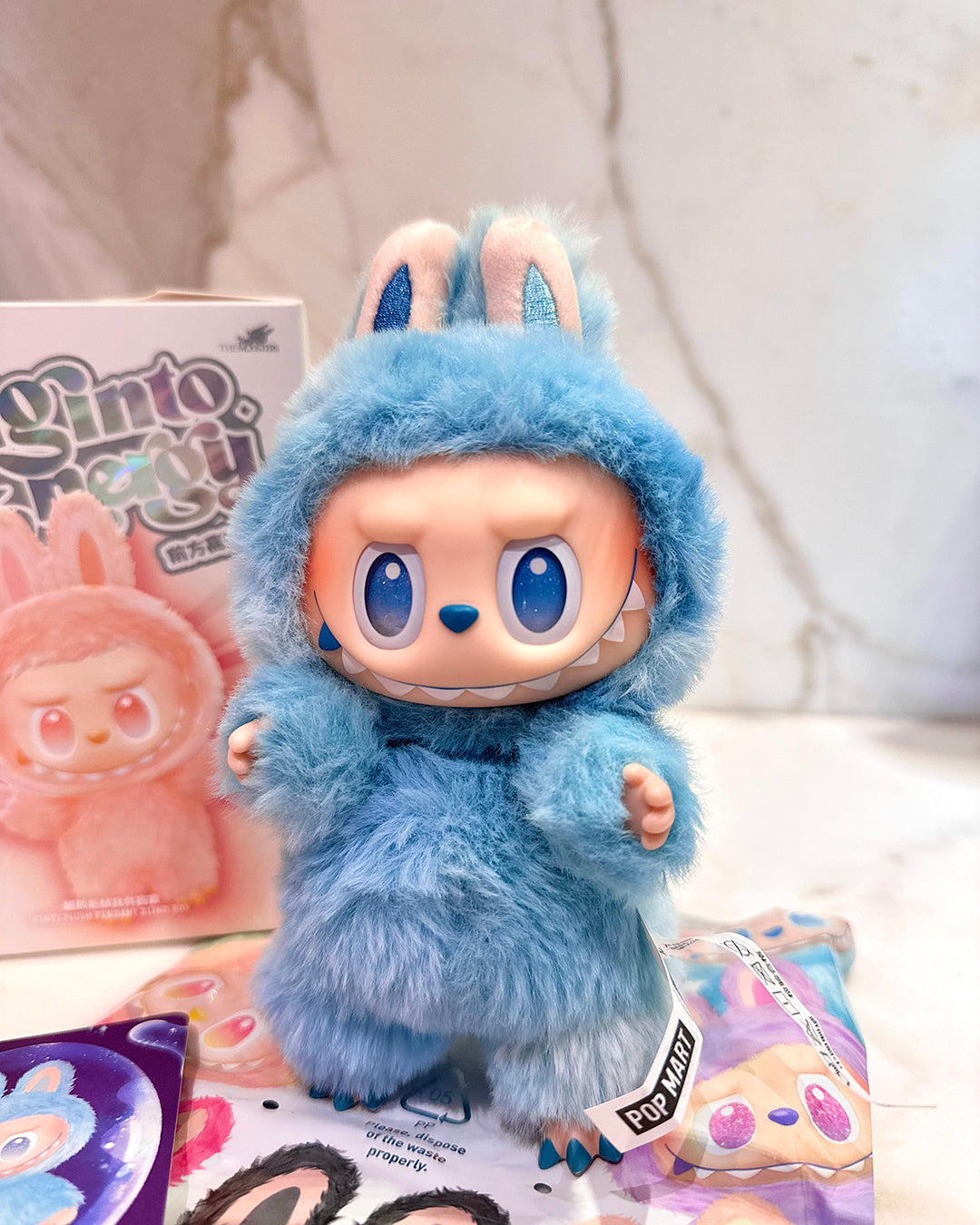 Blue plush toy with bunny ears on a white surface with packaging in the background