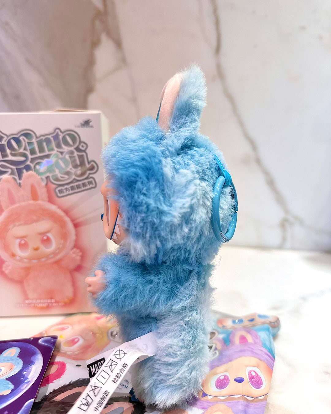 Blue plush toy with a book and colorful packaging in the background